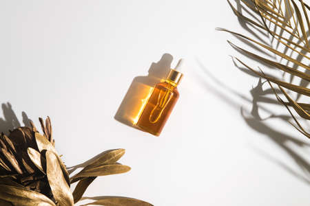 White, orange and black serum bottles on white background. Trending golden branches of palm and protea. Cosmetic mockup. Place to insert text, images. Top view. Flat lay.の写真素材