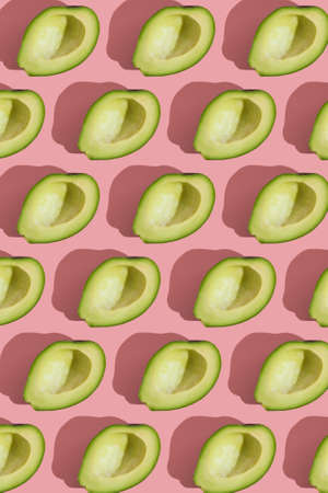 Trending style pattern of half seedless green avocado on pink background with hard light. Creative...
