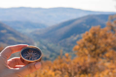 Female hand of traveler, hiker with compass on background autumn forest landscape with mountains on the horizon in orange colors in fall.の写真素材