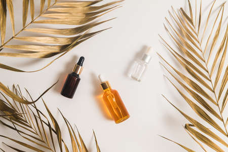 White, orange and black serum bottles on white background. Trending golden branches of palm. Cosmetic mockup. Place to insert text, images. Top view. Flat lay.の写真素材