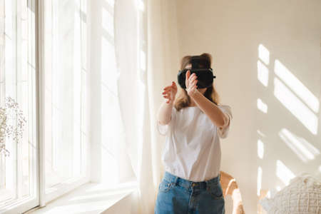 Young beautiful woman in white t-shirt and blue jeans plays game, dances with virtual reality...