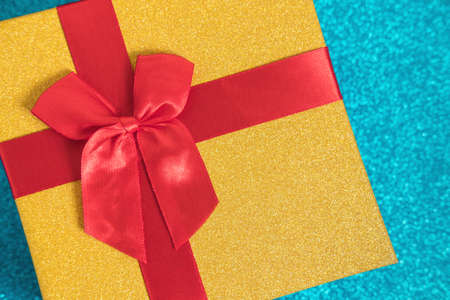 Golden glittering gift box withred bow on sparkling blue glitter background. Christmas and New Year background for congratulations on the coming holidays. Gift exchange. Flat lay. Top view. Copyspace.の写真素材