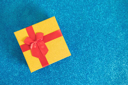 Golden glittering gift box withred bow on sparkling blue glitter background. Christmas and New Year...
