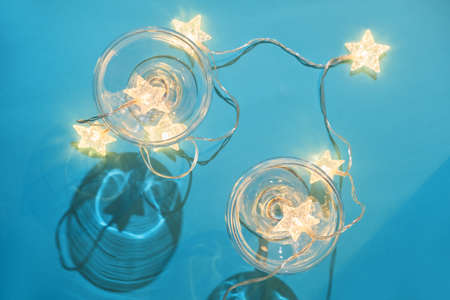 Christmas minimal festive background with star garland in glasses of champagne. Abstract Christmas and New Year color background blue ai aqua. Bright sparkling wallpaper. Top view.の写真素材