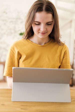 Young beautiful woman in yellow t-shirt usimg tablet for work, online business, studying sitting at home. Self-isolation, study, work during quarantine, pandemic. Remote job, education, student.の写真素材