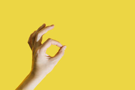 Female hand folded into a symbol okay on a bright yellow illuminating background. Trendy color of the year 2021.の写真素材