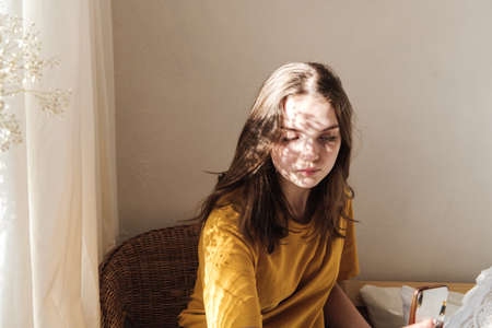 Portrait of young beautiful woman by the window with shadow from flowers on her face. Morning spring aesthetics.の写真素材