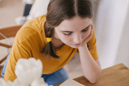 Young beautiful woman in yellow t-shirt engaged in work, online business, studying sitting at table at home. Self-isolation, study, work during quarantine, pandemic. Remote job, education, student.の写真素材