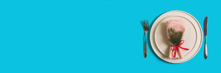 Banner with served table with empty plate and cutlery for celebration of Christmas and New Year. On plate is napkin with Christmas tree branch. Flatlay banner on bright blue background. Top view.の写真素材
