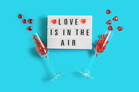 Festive background with glowing lightbox with text Love is in the Air and champagne glasses with red hearts on blue background for Valentines Day. Flatlay for 14th February. Top view.の写真素材