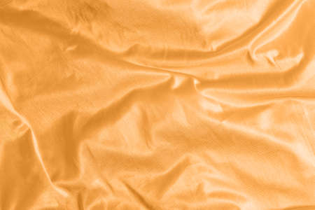 Shiny satin silk fabric with folds background texture textile. Tinted in 2021 color orange marigold.の写真素材