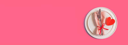 Banner with served table with plate and cutlery for the celebration of Valentines Day. On the plate is napkin with paper heart. Flatlay website banner on bright pink background. Top view.の写真素材