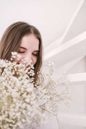 Portrait of young beautiful woman by the window with shadow from flowers on her face. Morning spring aesthetics.の写真素材
