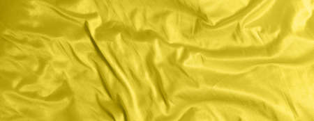 Shiny satin silk fabric with folds background texture textile. Tinted color yellow Illuminating.の写真素材