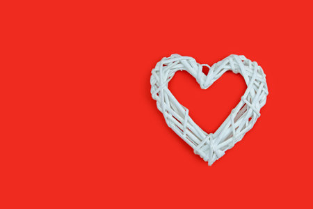 White wicker heart symbol lies on the red background to Valentines Day. Top view. Flat lay. Greeting card, concept of the holiday of lovers.の写真素材