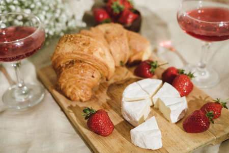 Cozy spring or summer picnic at home. Romantic picnic for Valentines Day on February 14 with croissant, strawberries, cheese and rose champagne. Protea and gypsophila flower.の写真素材