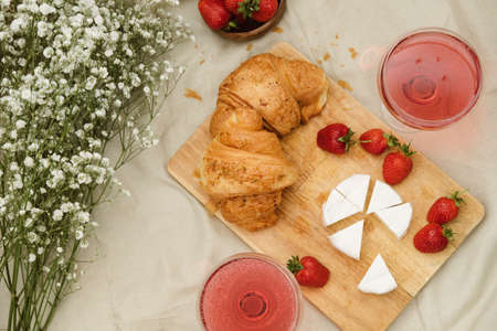 Cozy spring or summer picnic at home. Romantic picnic for Valentines Day on February 14 with croissant, strawberries, cheese and rose champagne. Protea and gypsophila flower.の写真素材