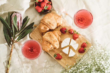 Cozy spring or summer picnic at home. Romantic picnic for Valentines Day on February 14 with croissant, strawberries, cheese and rose champagne. Protea and gypsophila flower.の写真素材