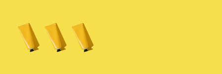 Thee yellow tube of sunscreen banner on bright yellow background with hard shadow. Sun protection in the summer.の写真素材