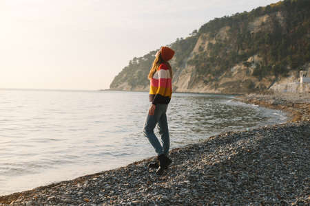 Young beautiful woman in striped sweater stands on the seashore or ocean and enjoy the view. Concept of freedom, thoughtfulness, mindfulness.の写真素材