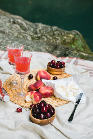 Cozy summer picnic near the lake with wine, cherry, peaches, brie cheese, camamber. Romantic picnic for Valentines Day on February 14.の写真素材