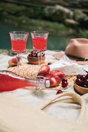 Cozy summer picnic near the lake with wine, cherry, peaches, brie cheese, camamber. Romantic picnic for Valentines Day on February 14.の写真素材
