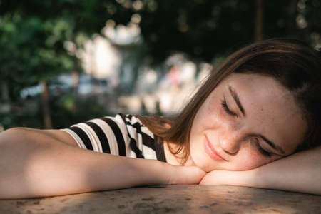 Portrait of a young lovely woman with blue eyes and freckles in a striped T-shirt and jeans sits on chair and enjoying sun.の写真素材