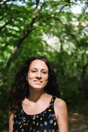 Beautiful woman with curly hair, half of her face is hidden behind tree. Unity with nature.の写真素材