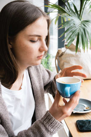 Young beautiful woman with freckles and blue eyes drinks coffee in a cafe.の写真素材