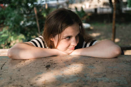 Portrait of a young lovely woman with blue eyes and freckles in a striped T-shirt and jeans sits on...