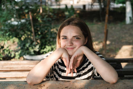 Portrait of a young lovely woman with blue eyes and freckles in a striped T-shirt and jeans sits on chair and enjoying sun.の写真素材