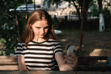 Portrait of a young lovely woman with blue eyes and freckles in a striped T-shirt and jeans sits on chair and makes a selfie.の写真素材