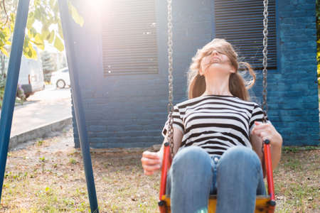 Young lovely woman in a striped T-shirt and jeans is riding a swing and laughing.の写真素材