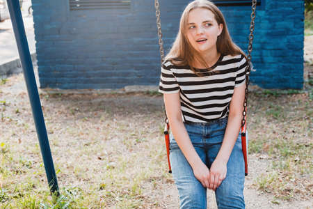 Young lovely woman in a striped T-shirt and jeans is riding a swing and laughing.の写真素材