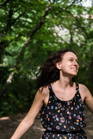 Beautiful woman with curly hair, half of her face is hidden behind tree. Unity with nature.の写真素材