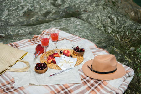 Cozy summer picnic near the lake with wine, cherry, peaches, brie cheese, camamber. Romantic picnic for Valentines Day on February 14.の写真素材