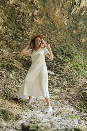 Beautiful woman in white long dress and hat is standing in forest on the stone. Travel concept.の写真素材