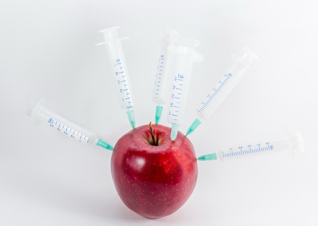 Apple in a medical syringe on a gray background. Introduction to fruit chemicals, nitrates.の写真素材