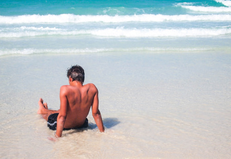 back view of young man has tan skin is sitting on the beachの写真素材