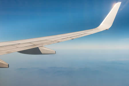 Wing of the plane on blue sky background and mountains belowの写真素材
