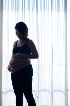 woman pregnant standing near curtain, shot in a dark toneの写真素材