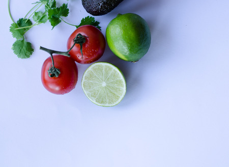 Avocado, lime cut in half, tomatoes on the vine and cilantro/koriander placed in a group on a white backgroundの写真素材