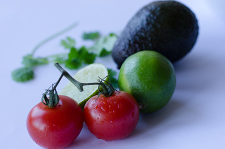 Avocado, lime cut in half, tomatoes on the vine and cilantro/koriander placed in a group on a white backgroundの写真素材