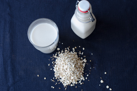 A bottle of oat milk with a glass of the same beside it.の写真素材