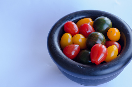 A variety of tomatoes in group in a bowl of stone on white backgroundの写真素材