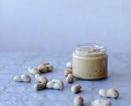 Homemade peanut butter in glass jar with peanuts spread on the table
