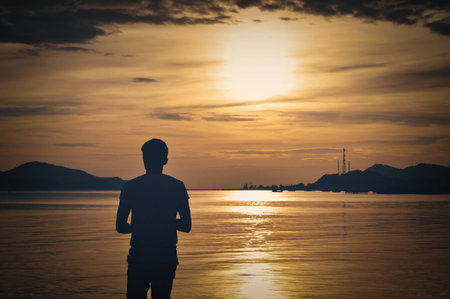 Lonely Asian Man Silhouette Standing In Front Of Golden In Evening Sunset Seascape Viewの写真素材