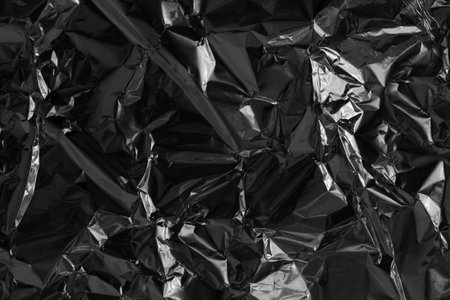 Shiny black foil texture background, pattern of wrapping paper with crumpled and wavy.