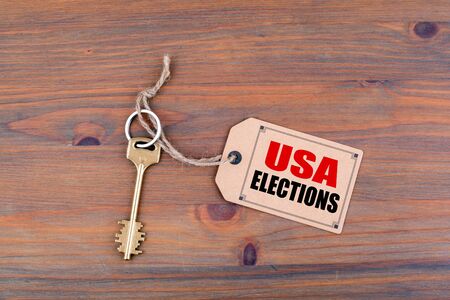Key and a note on a wooden table with text: USA Elections.
