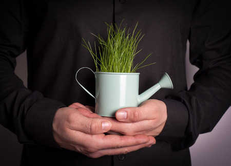Human hand holding Miniature watering pot with fresh green spring grass. Abstract background for business and development.の写真素材